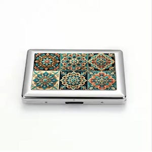 Puede incluir: Un estuche de cigarrillos de metal plateado con un diseño de mosaico decorativo. El mosaico se compone de seis cuadrados, cada uno con un patrón floral único en verde azulado, naranja y dorado. El estuche tiene forma rectangular.