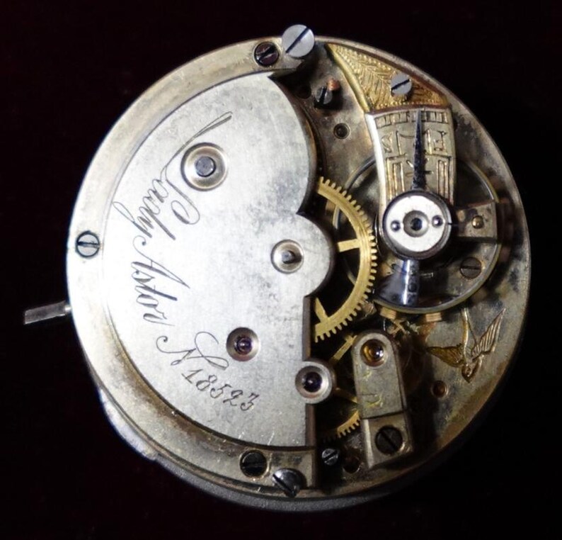 May include: Close-up of a vintage watch movement with intricate gears, screws, and a balance wheel. The watch mechanism has a silver-colored plate with the inscription "Lady Astor" and the number "18593". The design includes gold-colored accents and a decorative bird.