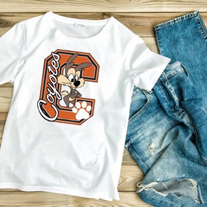 May include: White t-shirt with an orange and brown letter C and the word "Coyotes" in a brown script font. A cartoon coyote is inside the letter C.