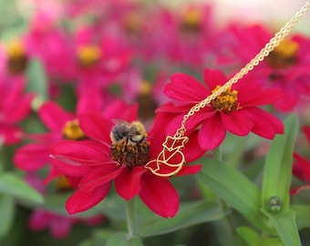 Puede incluir: Un collar de oro con un colgante de zorro cuelga de una flor rosa. Una abeja está posada en la flor.