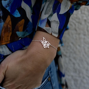 May include: A silver bracelet with a delicate, intricate design. The design resembles a stylized knot or a series of intertwined shapes.
