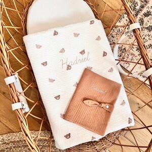 May include: A white woven basket with a white and brown baby blanket with a bear pattern and the name Hadriel embroidered on it. A brown muslin cloth with the name Hadriel embroidered on it is on top of the blanket.