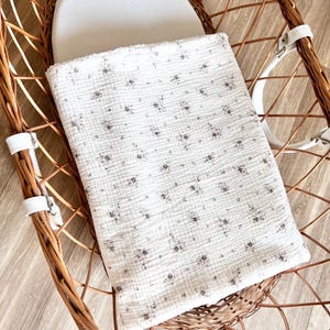 May include: A white wicker bassinet with a white cotton liner and a white and gray floral patterned blanket.