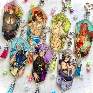 May include: A collection of anime-style character keychains. Each keychain features a unique character design with vibrant colors, attached to a silver heart-shaped clasp and a tassel. The characters have various hair colors and outfits.