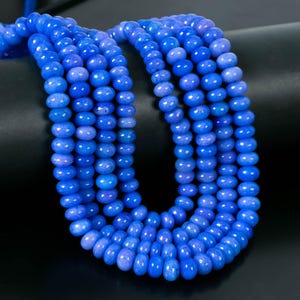 May include: Close-up of multiple strands of blue gemstone beads. The beads are a vibrant shade of blue, with a polished, faceted surface. The beads are strung together, creating a necklace or bracelet.