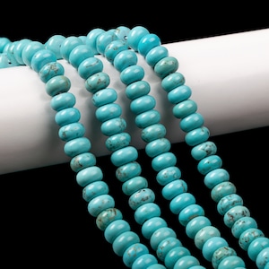 May include: A strand of turquoise beads, with a light blue color and a smooth, round shape. The beads are arranged in a row, with the ends of the strand visible. The beads are on a white surface.