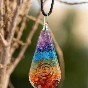 May include: A teardrop-shaped pendant necklace with a seven-chakra design. The pendant is made of clear resin with embedded crystals in various colors, including purple, blue, green, yellow, orange, and red. A copper wire spiral is embedded in the center of the pendant.