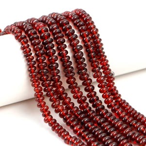 May include: A collection of multiple strands of deep red, translucent, disc-shaped beads arranged in parallel lines. Each strand consists of numerous small, uniform, circular beads with a smooth, polished finish, creating a vibrant, rich color.