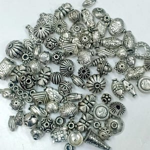 May include: A large assortment of silver-toned metal beads with various shapes and designs. The beads are perfect for jewellery making, crafting, and DIY projects.