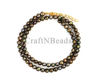 May include: A necklace composed of round, dark-toned iridescent pearls with a metallic sheen. The strand features a gold-toned metal clasp and an adjustable chain extension. The text CraftNBeads is overlaid in the center of the circular arrangement.