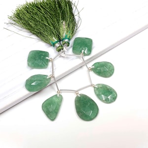 Pode incluir: Um fio de contas de pedras preciosas verdes com um conector de prata. As contas são facetadas e têm uma variedade de formas, incluindo quadrada, oval e em forma de lágrima. O fio é terminado com um tassel verde.