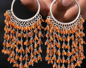 May include: A pair of silver hoop earrings featuring multiple dangling chains adorned with small, round, translucent orange carnelian beads. The beads are arranged in a tiered fringe pattern hanging from the bottom half of each circular silver hoop.