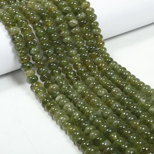 May include: A strand of green gemstone beads, each bead is round and smooth. The beads are strung together on a clear thread. The beads are all approximately the same size and shape.