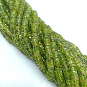 May include: A strand of green peridot beads, faceted and polished, with a square shape. The beads are strung together on a clear thread.