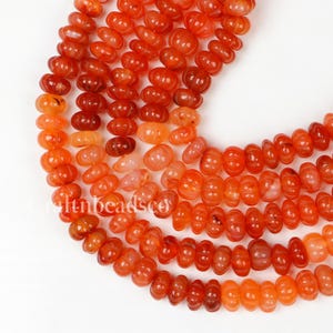 May include: Close-up of strands of orange-red gemstone beads. The beads have a pumpkin shape and are strung together. The colour varies from light orange to deep red. The beads are likely used for jewellery making.