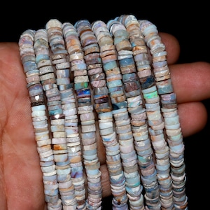 Puede incluir: Una hebra de cuentas de ópalo multicolores, con una mezcla de tonos blancos, marrones y azules. Las cuentas son pequeñas y redondas, y están enhebradas en un hilo transparente.