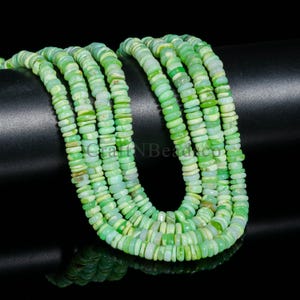May include: Strands of green and white gemstone beads. The beads are flat, disc-shaped, and vary in shades of green. The beads are strung together, creating a layered effect. The background is black.
