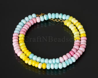 May include: A circular necklace composed of small, smooth, disc-shaped beads in alternating pastel shades of light blue, soft pink, and bright yellow. The strand is secured with a gold-toned metal clasp, creating a continuous, colorful loop.