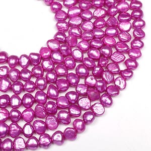 May include: A strand of pink freshwater pearls. The pearls are irregular in shape and have a high luster. They are strung on a clear thread.