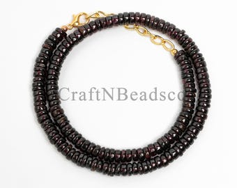 May include: A necklace made of dark red beads with a gold-colored clasp. The beads are small and round, strung together to form a necklace. The necklace is displayed on a white background. The text "CraftNBeadsco" is visible.