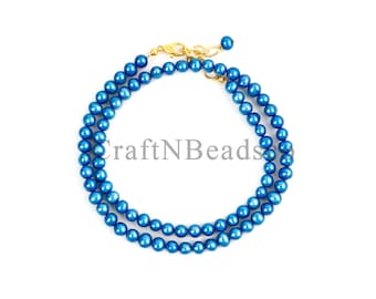May include: A double-strand necklace featuring round, vibrant blue beads with a polished finish. The necklace is secured with a gold-toned metal lobster claw clasp and a short extender chain. The text CraftNBeads is centered over the blue beads.