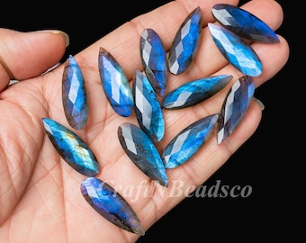 May include: A collection of marquise-shaped labradorite gemstones featuring faceted surfaces and iridescent blue flashes. Each stone displays a dark gray base with vibrant blue and gold light reflections. The text CraftNBeadsco is visible.