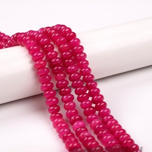 May include: A strand of pink jade beads, with a smooth, round shape. The beads are strung on a white cord and are arranged in a row.