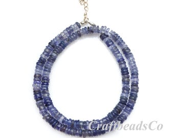 May include: A necklace composed of two strands of small, flat, circular blue beads in varying shades of indigo and periwinkle. The necklace features a silver-toned metal clasp and an adjustable extender chain. The text CraftbeadsCo is visible.