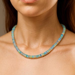 May include: A beaded necklace with a gradient of colors, including blue, green, and yellow. The necklace is composed of small, round beads and is worn around the neck.