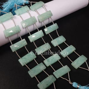 May include: Strands of rectangular, light blue-green gemstone beads. Each bead is connected by silver-coloured wire. The beads have a faceted surface. The image also shows a blue tassel and the text "Craftnbeadsco".