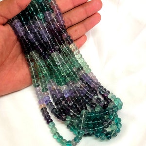 Può includere: Una collana di perle di fluorite verde, viola e blu. Le perle sono rotonde e hanno una finitura liscia e lucida.