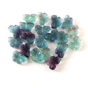 May include: A collection of 18 butterfly-shaped beads made of fluorite. The beads are a mix of blue, green, and purple colors.
