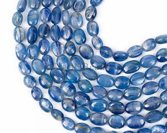 May include: A strand of oval-shaped blue kyanite gemstone beads. The beads are smooth and polished, with a light blue color and a slight shimmer.