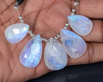 May include: A strand of five pear-shaped moonstone beads. The beads are faceted, displaying a play of blue and white colors. Each bead is strung with silver-colored beads and black cord.