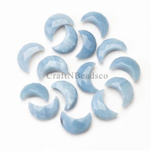 Può includere: Una collezione di 12 perle di pietra preziosa di forma a mezzaluna di colore blu chiaro. Le perle sono lisce e lucidate, con una finitura leggermente iridescente.