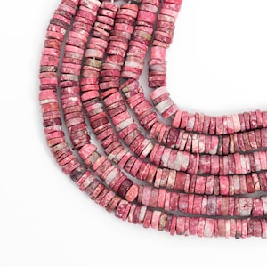Könnte beinhalten: Nahaufnahme von Strängen aus rosa und weißen Edelsteinperlen. Die Perlen sind flach, rechteckig und aufgefädelt. Die Farbpalette umfasst Rosa-, Weiß- und Grautöne. Die Perlen sind in einem gebogenen Muster vor einem weißen Hintergrund angeordnet.