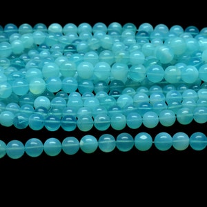 May include: A strand of round, light blue gemstone beads. The beads are smooth and polished, with a translucent appearance.