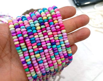May include: A collection of colorful beaded strands in shades of pink, purple, blue, green, and yellow. The beads are small and round, and the strands are held in a hand. The beads are likely used for jewelry making.