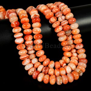 May include: Strands of orange and white gemstone beads. The beads are oval-shaped and strung together, creating a necklace-like appearance. The beads have a polished finish and vary in color, with some displaying striped patterns.
