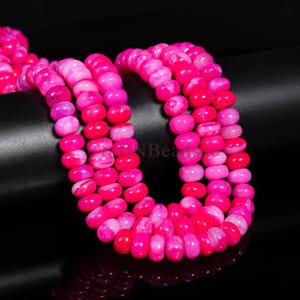 May include: Close-up of several strands of pink gemstone beads. The beads are a mix of solid and marbled pink hues, creating a layered effect. The oval-shaped beads are strung together, ideal for crafting jewellery.