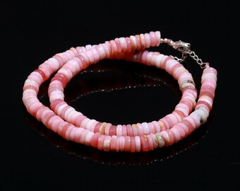 May include: A necklace composed of small, flat, disc-shaped beads in varying shades of pink, ranging from pale blush to deep rose. The beads are strung together in a continuous circular pattern, finished with a silver-toned metal lobster claw clasp.