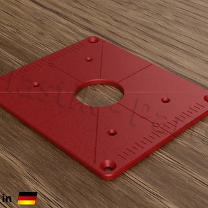 May include: Red square router table insert with a large center hole and several smaller holes around the perimeter. The insert has a ruler on two sides.