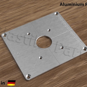 Peut inclure: Une plaque carrée en aluminium argentée avec un grand trou au centre et cinq petits trous autour du bord. La plaque est munie d'une règle graduée sur un côté. Le texte "Aluminium Platte" est imprimé en noir en haut de l'image.