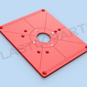 May include: Red plastic router table insert with a circular cutout and multiple holes for mounting. The insert has a ruler on two sides.