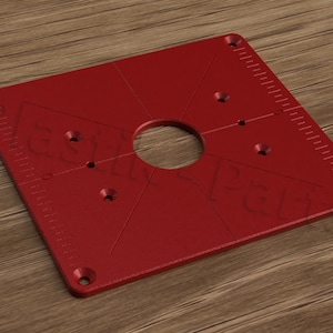May include: Red square router plate with a large center hole and multiple smaller holes around the perimeter. The plate has a ruler on one side.