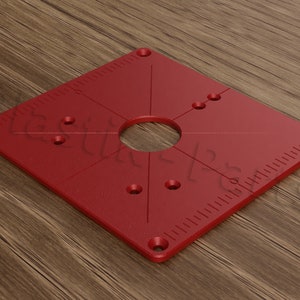 Peut inclure: Plaque d'insertion de table de toupie rouge avec un grand trou central et plusieurs petits trous pour le montage. La plaque a une règle sur le bord.