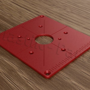 May include: Red square router template with a large centre hole and multiple smaller holes around the perimeter. The template has a ruler on two sides.