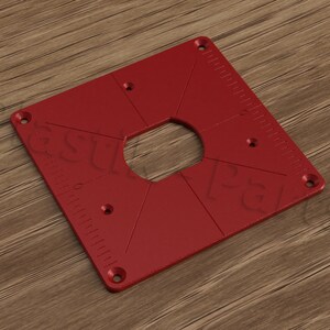 Può includere: Modello per fresatrice quadrato rosso con un grande ritaglio circolare e quattro fori più piccoli. Il modello ha un righello su un lato e il testo "PG" al centro.