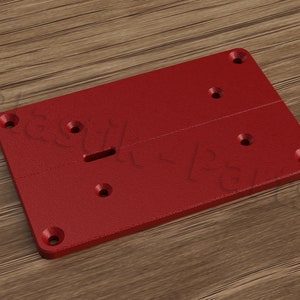 May include: A red plastic plate with five holes and a slot in the center. The plate is designed for mounting a device.