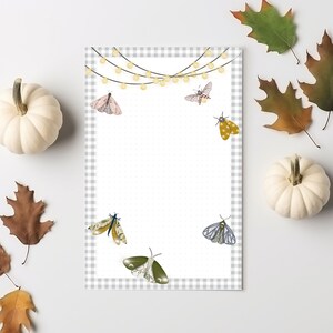 May include: A white sheet of paper with a gray and white gingham border. The paper is decorated with a string of lights and several colorful butterflies. The paper is perfect for journaling, note-taking, or creating to-do lists.